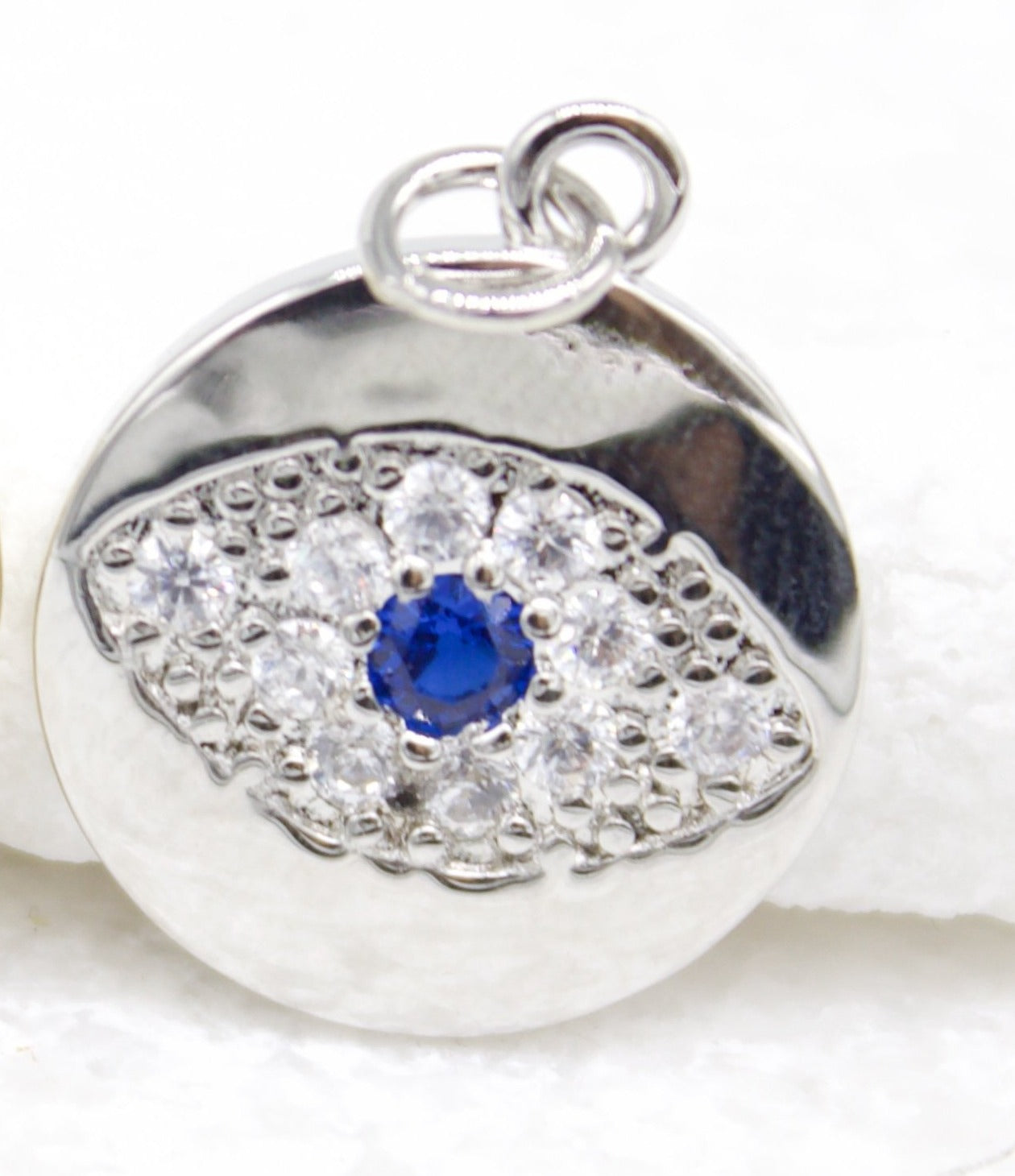 A silver evil eye pendant sparkles with pave-set cubic zirconia and a central blue sapphire stone.