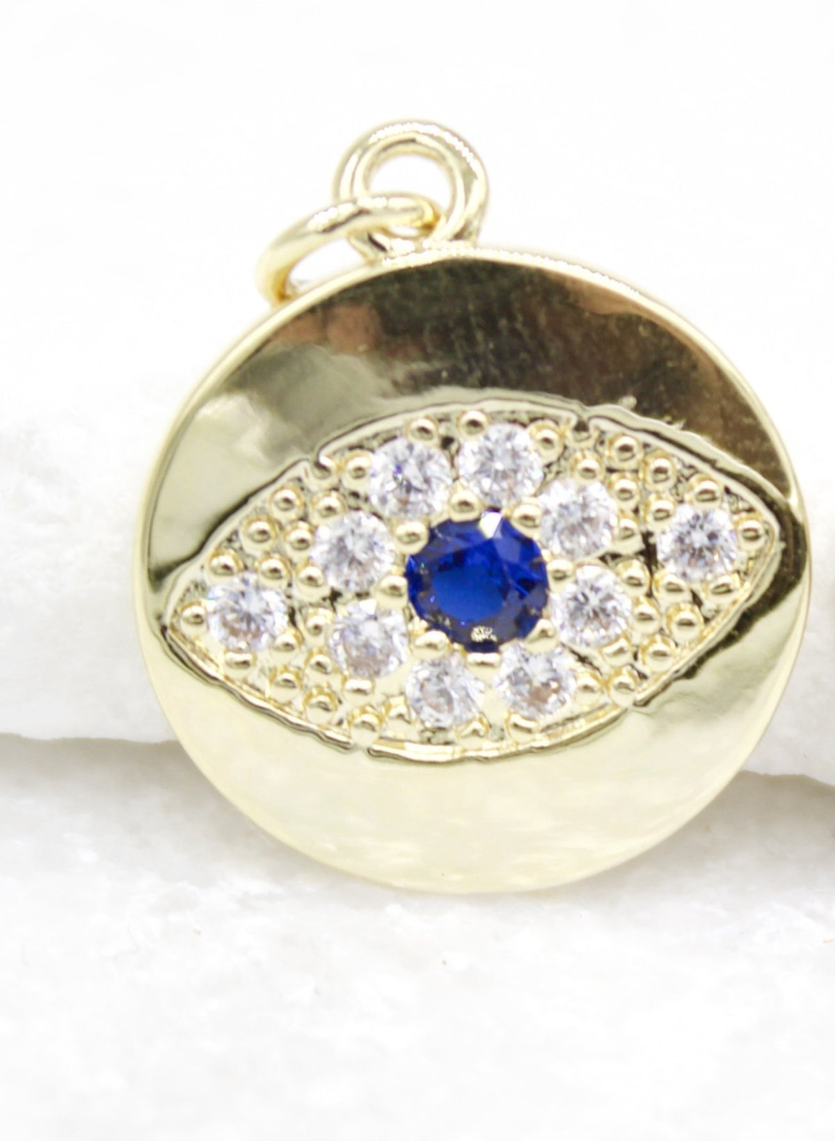 A round gold evil eye pendant gleams with a central blue sapphire surrounded by sparkling cubic zirconia stones.