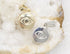 A gold evil eye pendant and a silver evil eye pendant rest side-by-side on a textured crystal surface.