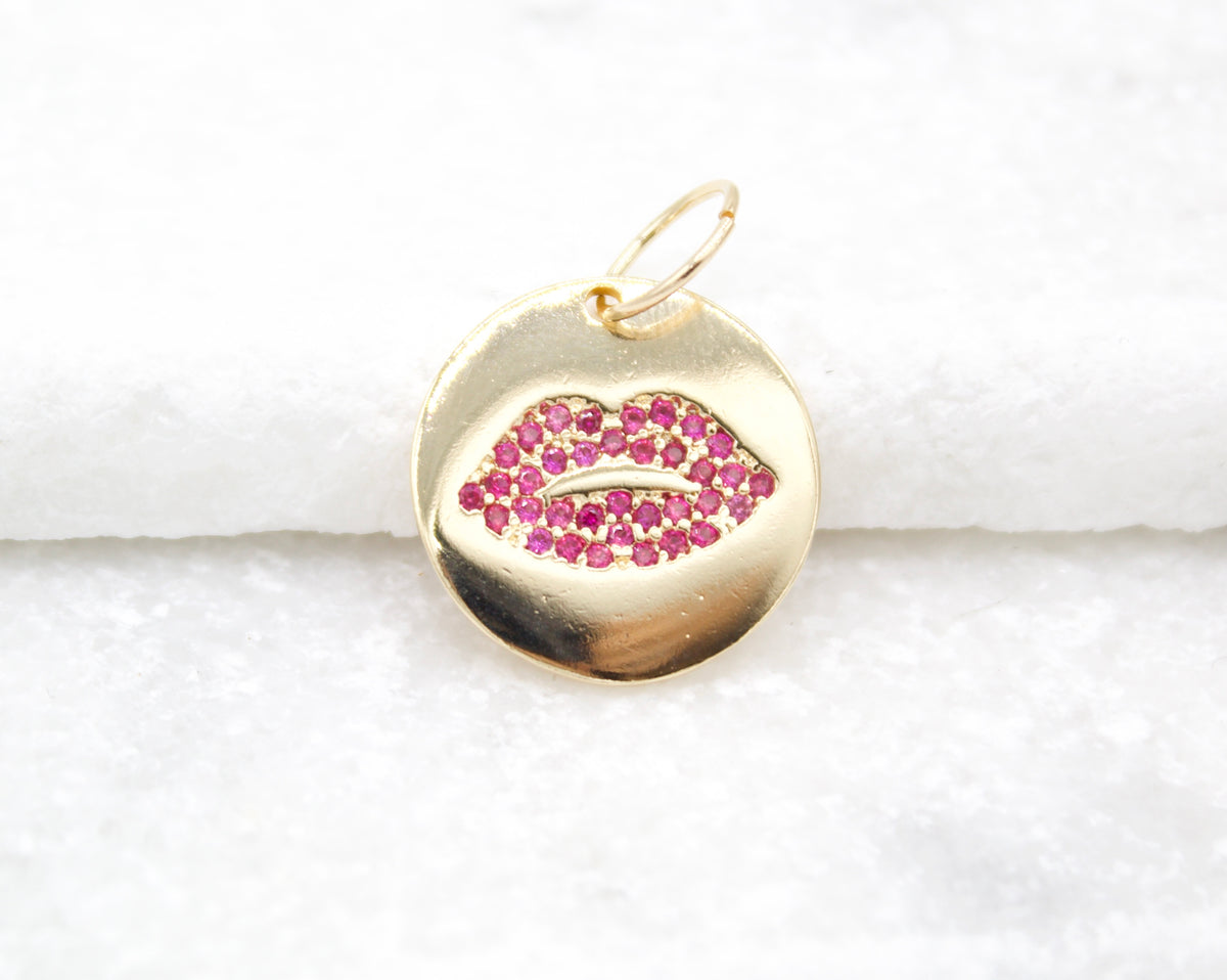 A round gold charm features an inset of sparkling pink cubic zirconia stones shaped like lips.