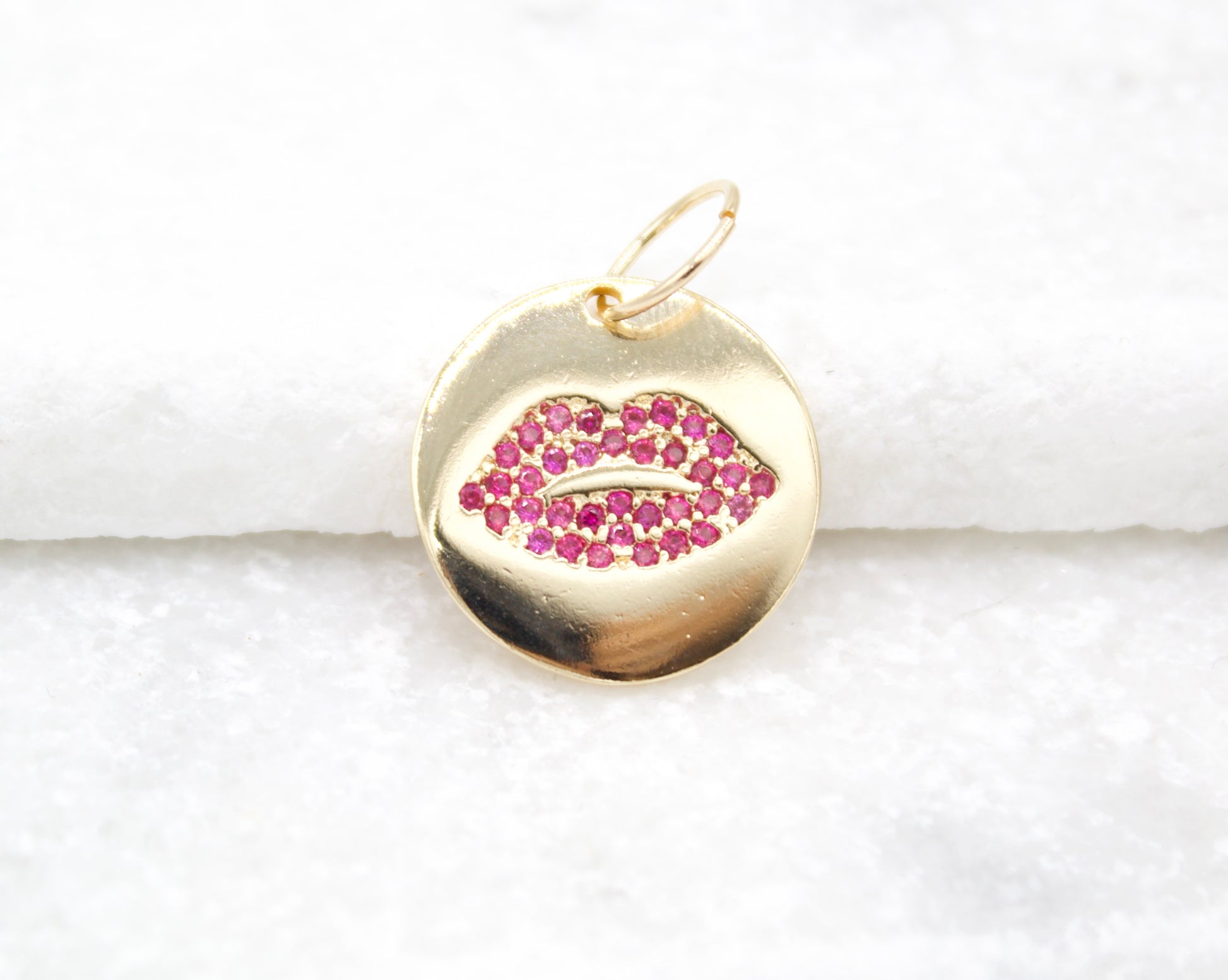 A round gold charm features an inset of sparkling pink cubic zirconia stones shaped like lips.