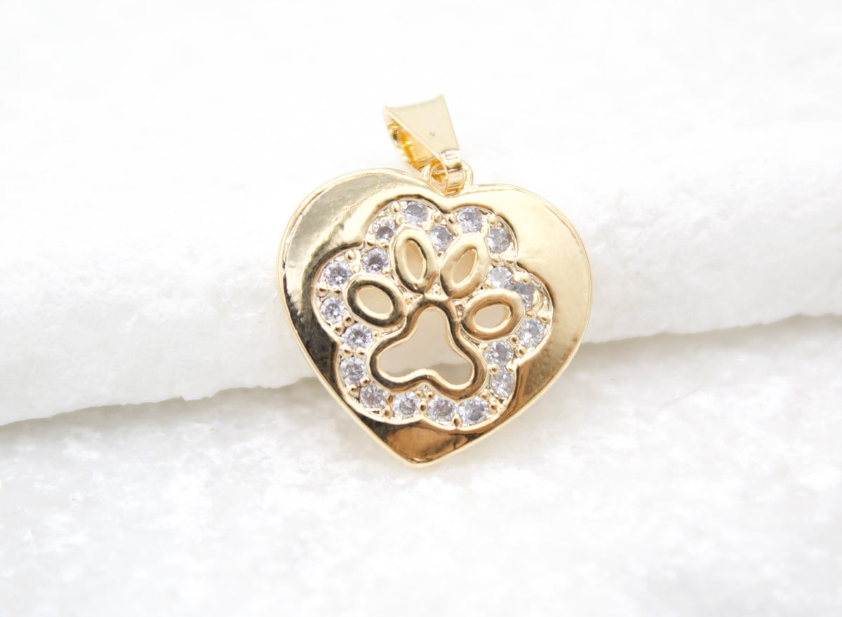 A gold heart pendant encrusted with sparkling cubic zirconia stones showcases an engraved paw print in the center.