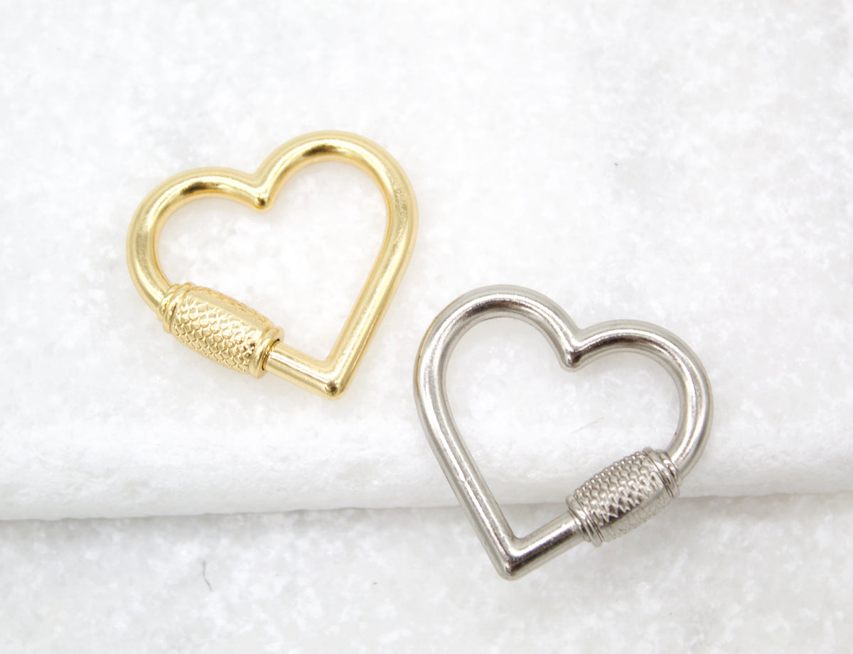 Two heart-shaped carabiner keychains in gold and silver rest on a white surface.