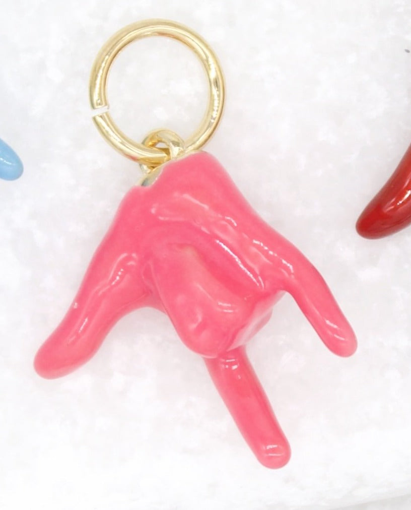 A glossy pink enamel hand charm shaped into the I love you sign hangs from a gold jump ring.
