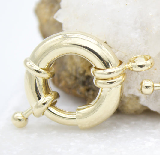 A polished gold spring ring clasp rests against a white crystal background.