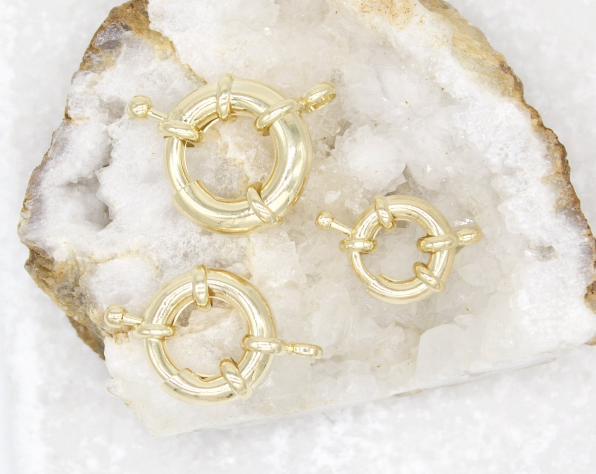 Three gold spring ring clasps rest on a sparkling white crystal geode.