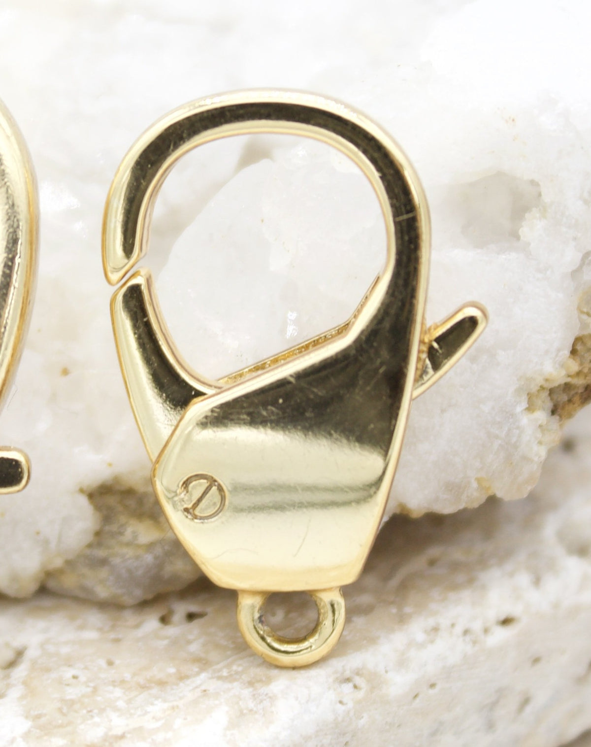 A close-up shot displays a gleaming gold lobster claw clasp resting against a textured white background.