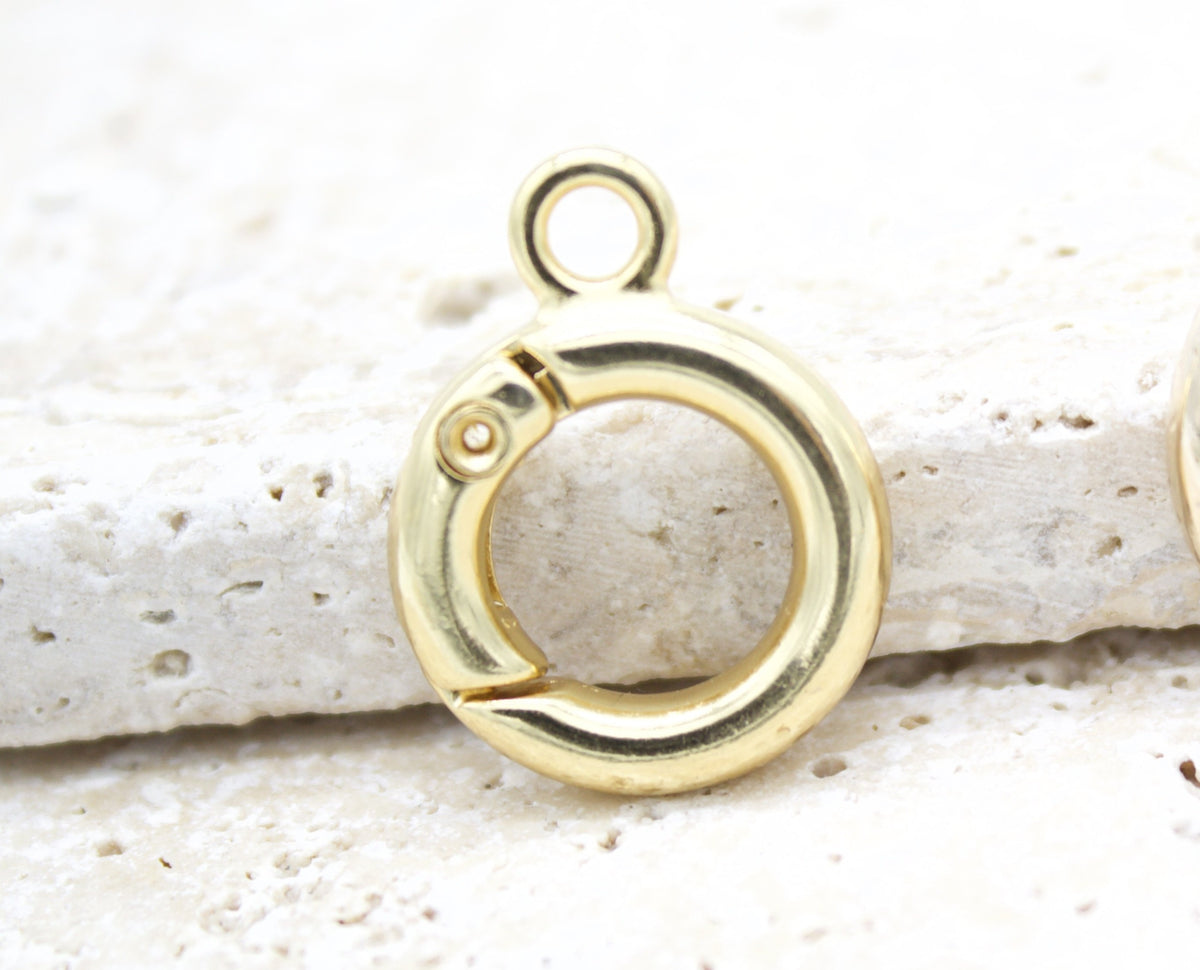A shiny gold spring ring clasp rests on a textured stone surface, showcasing its round shape and secure closure mechanism.