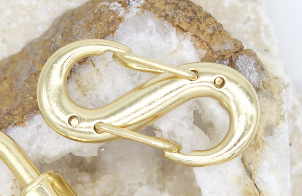 A shiny gold double-ended snap hook rests on top of a textured crystal stone background.