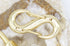 A shiny gold double-ended snap hook rests on top of a textured crystal stone background.