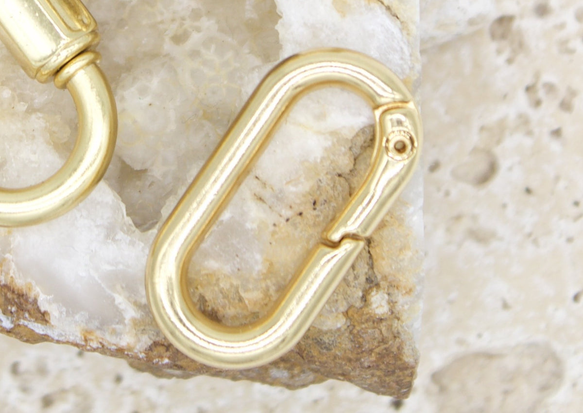 Two polished gold spring gate rings rest against a textured stone surface.