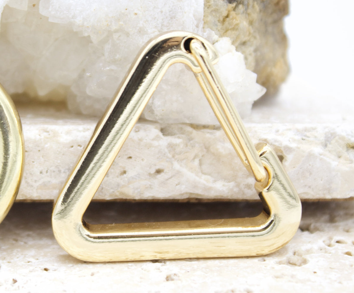 A shiny gold triangle charm rests on a textured white stone surface.