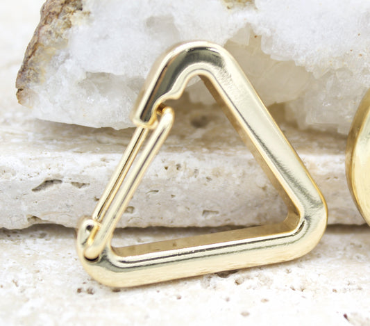 A polished gold triangular spring clasp rests against a textured white crystal background.