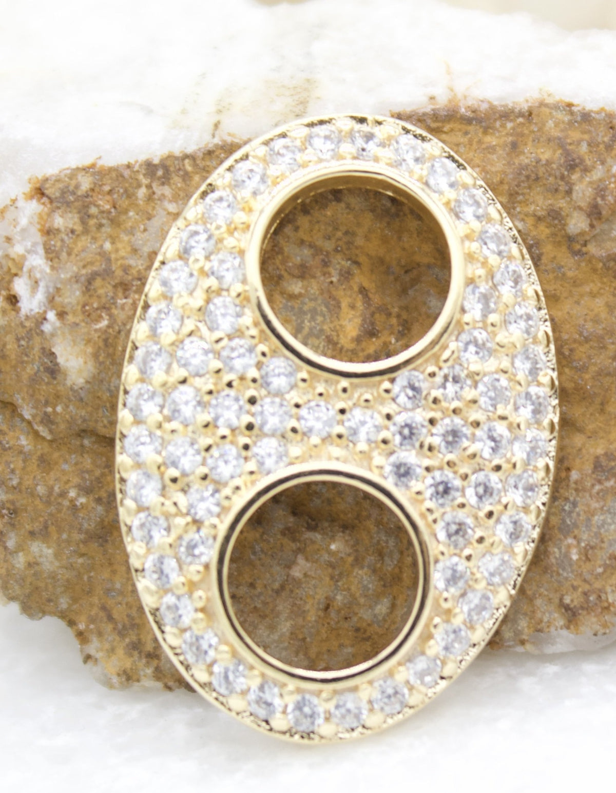 A gold pendant encrusted with sparkling cubic zirconia stones rests against a textured stone background.