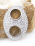 A sparkling pave-set diamond oval pendant rests on a textured stone surface, showcasing two central circular cutouts.