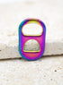 A vibrant iridescent rainbow soda tab rests upright on a textured stone surface.