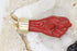 A carved red coral figa fist pendant featuring a gold cap rests against a bed of white quartz crystals.