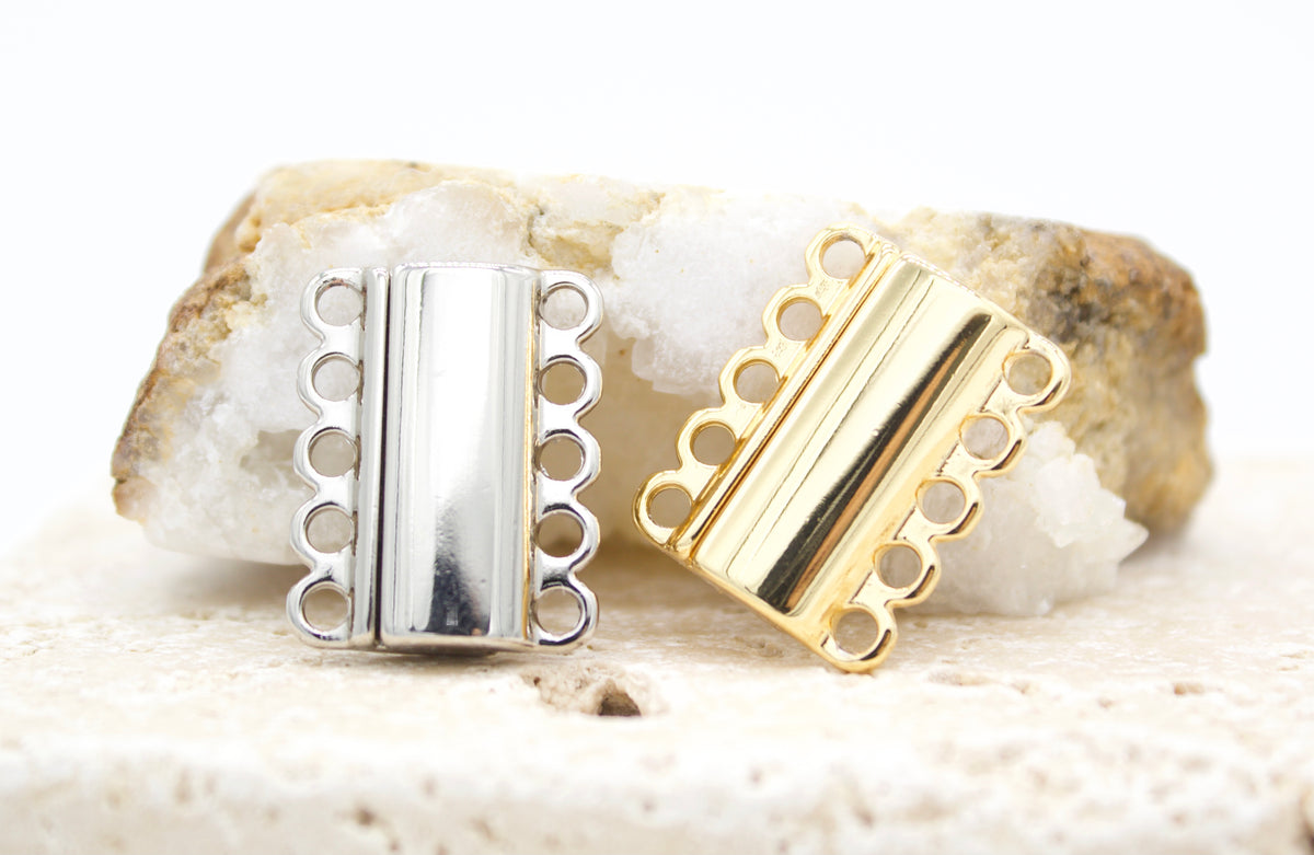 A silver and a gold multi-strand slide clasp rest against a textured quartz crystal background.