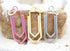 Three colorful paperclip charms in pink, gold, and silver display jump rings and rest upright against a textured stone backdrop.