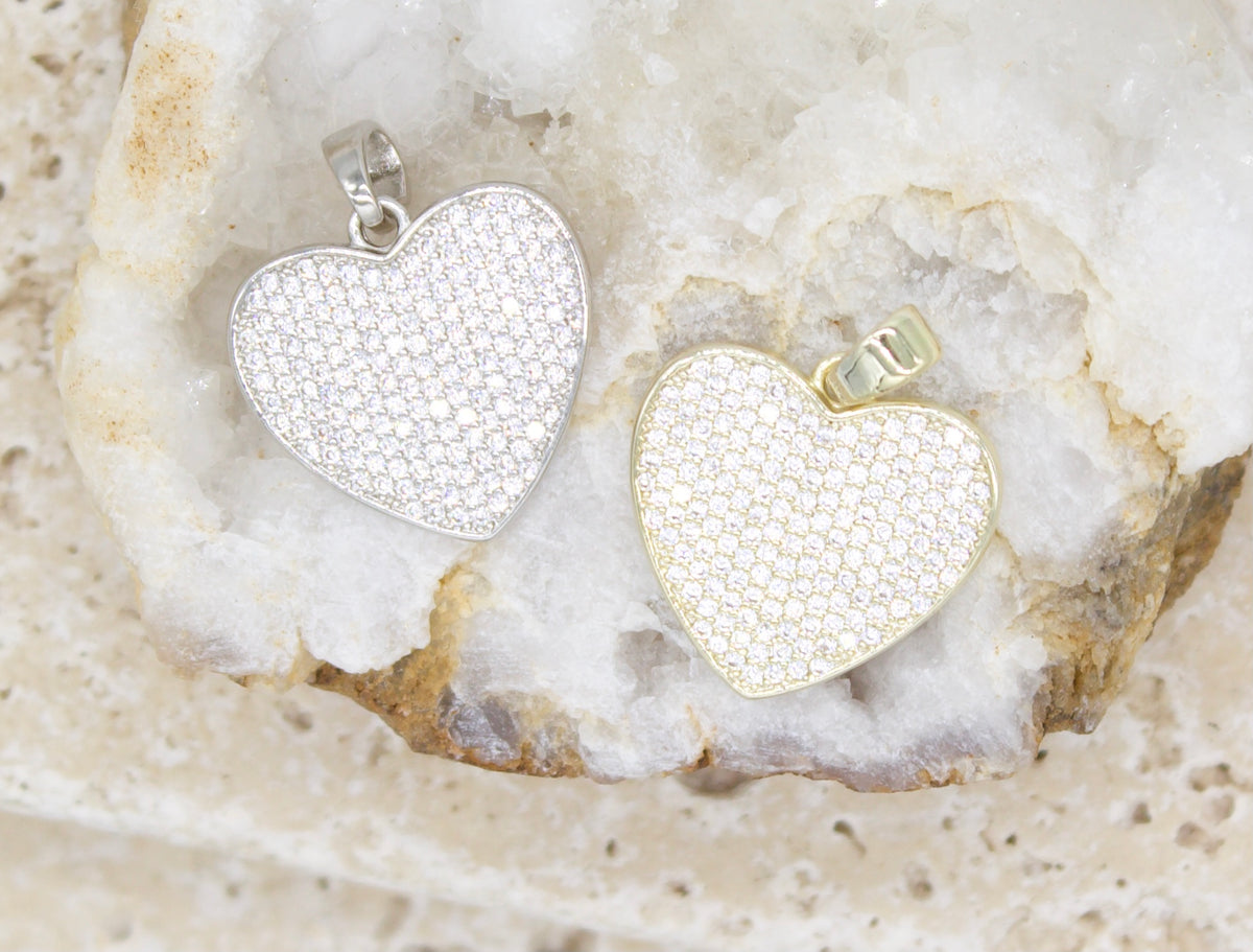 A silver and a gold pavé diamond heart pendant rest side by side inside a white crystal geode.