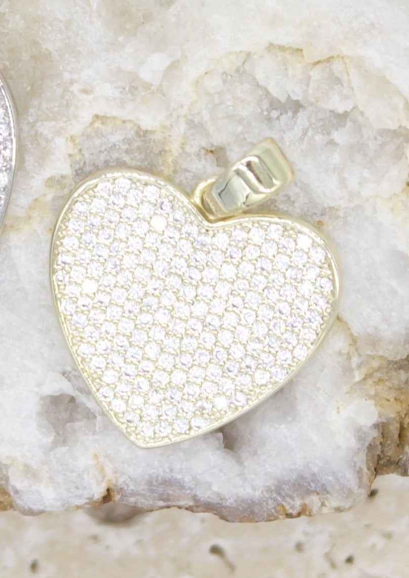A gold heart-shaped pendant encrusted with shimmering pavé diamonds rests on a textured white crystal surface.