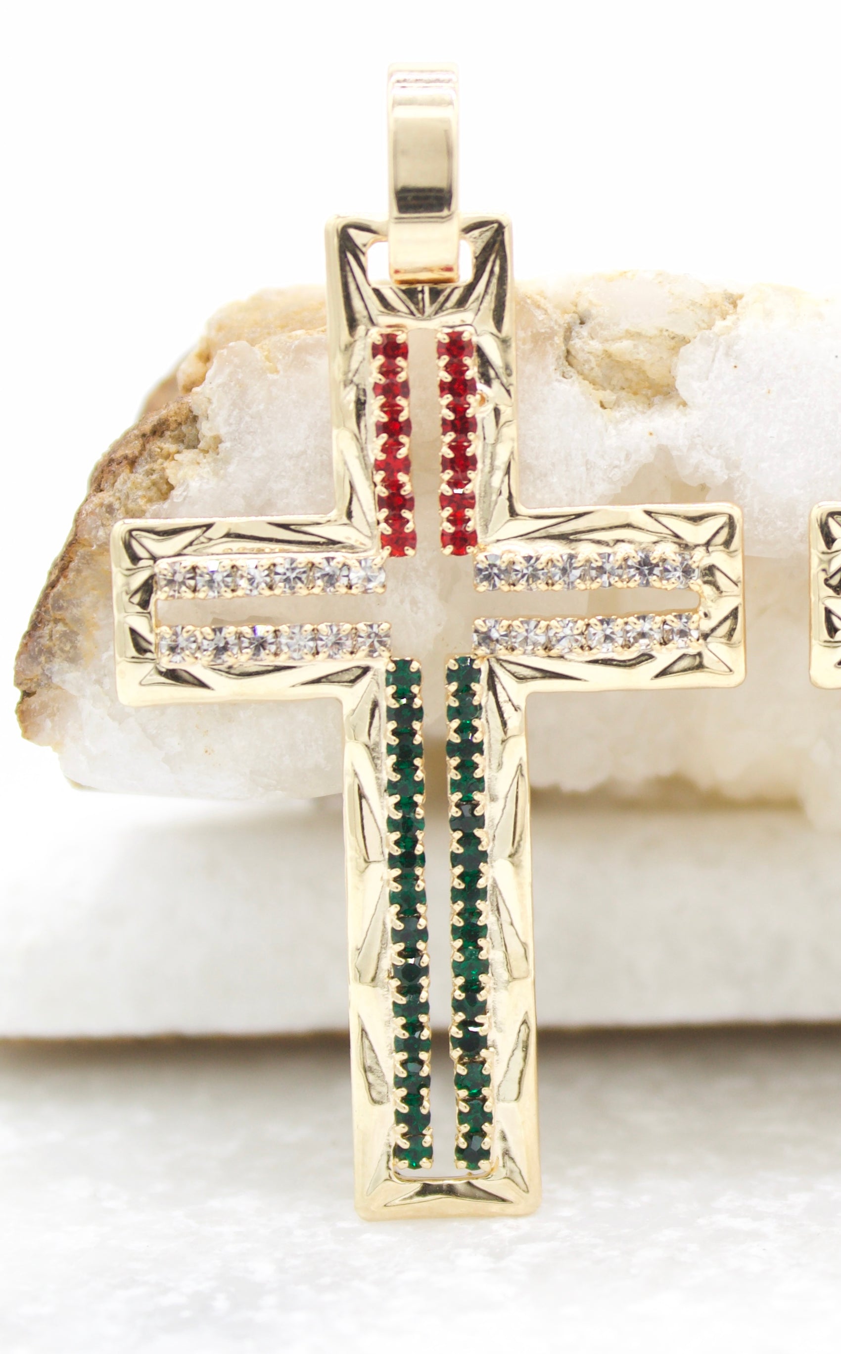 A gold cross pendant encrusted with red, white, and green gemstones rests against a white stone.