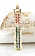 A gold cross pendant encrusted with red, white, and green gemstones rests against a white stone.