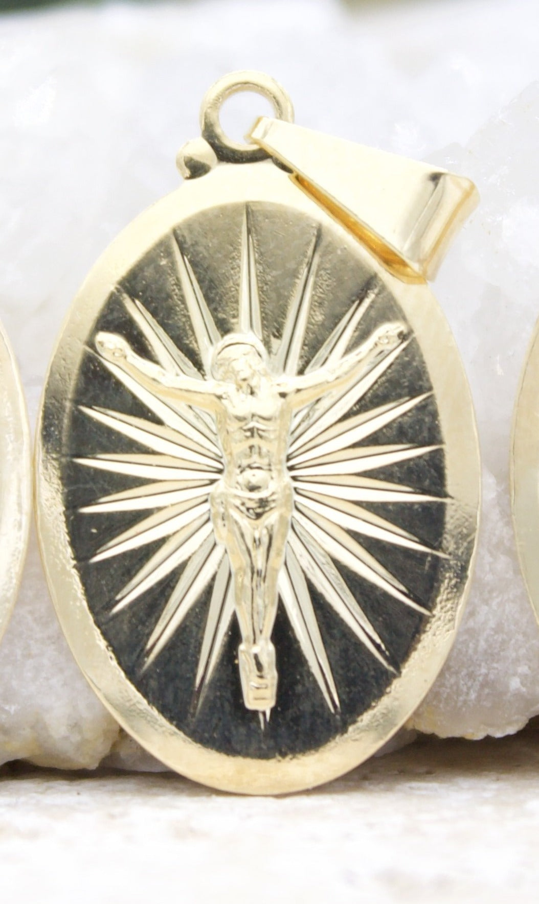 A gold crucifix pendant features an oval medallion depicting Jesus on the cross against a background of radiating sunburst rays.
