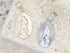 Two Our Lady of Guadalupe pendants, one in gold and one in silver, rest side by side on a textured stone surface.
