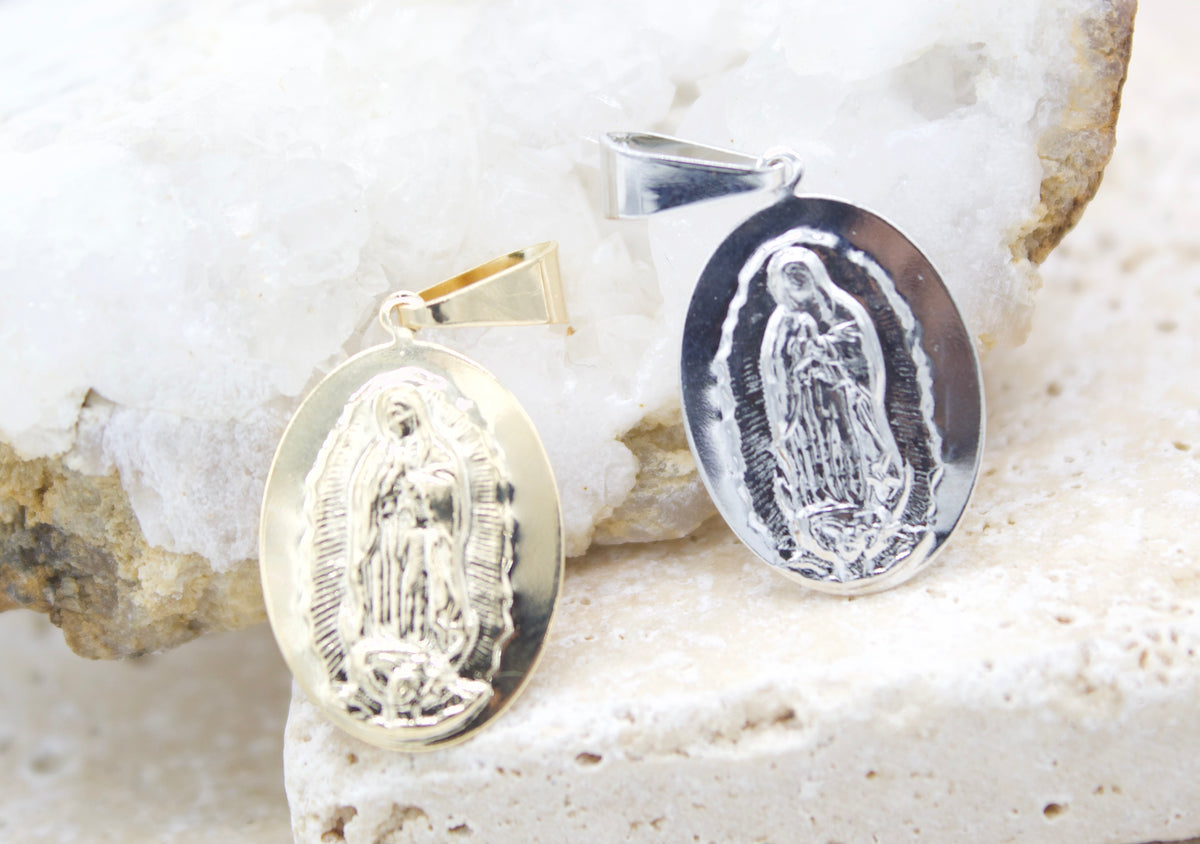 A gold and a silver Virgin Mary pendant rest on a white crystal and stone surface.