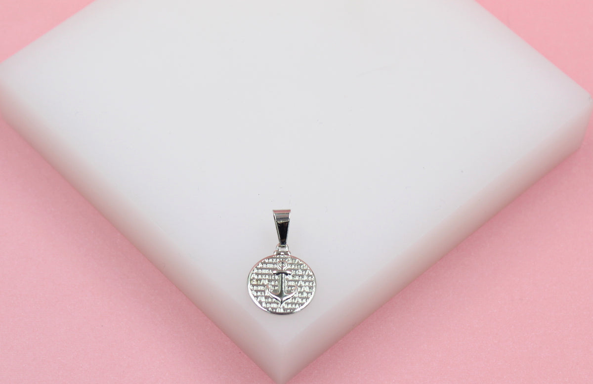 A silver anchor pendant rests on a white display block against a pink background.