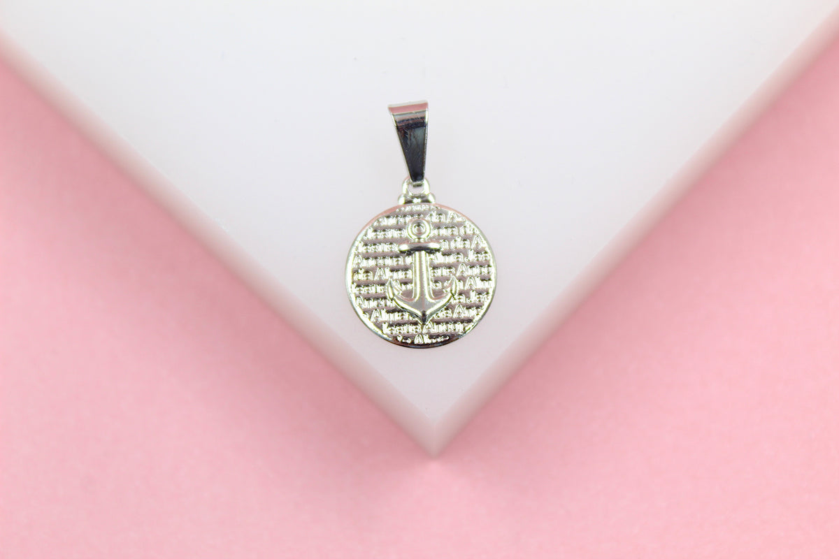 A silver pendant featuring an anchor design rests on a white display against a pink background.