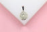 A silver pendant featuring an anchor design rests on a white display against a pink background.