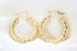 A pair of polished gold twist hoop earrings rests gracefully on a white silk background.