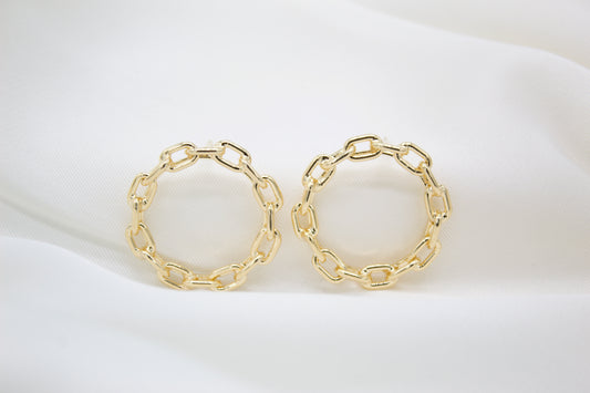 Two round gold chain-link hoop earrings rest on a white silk background.