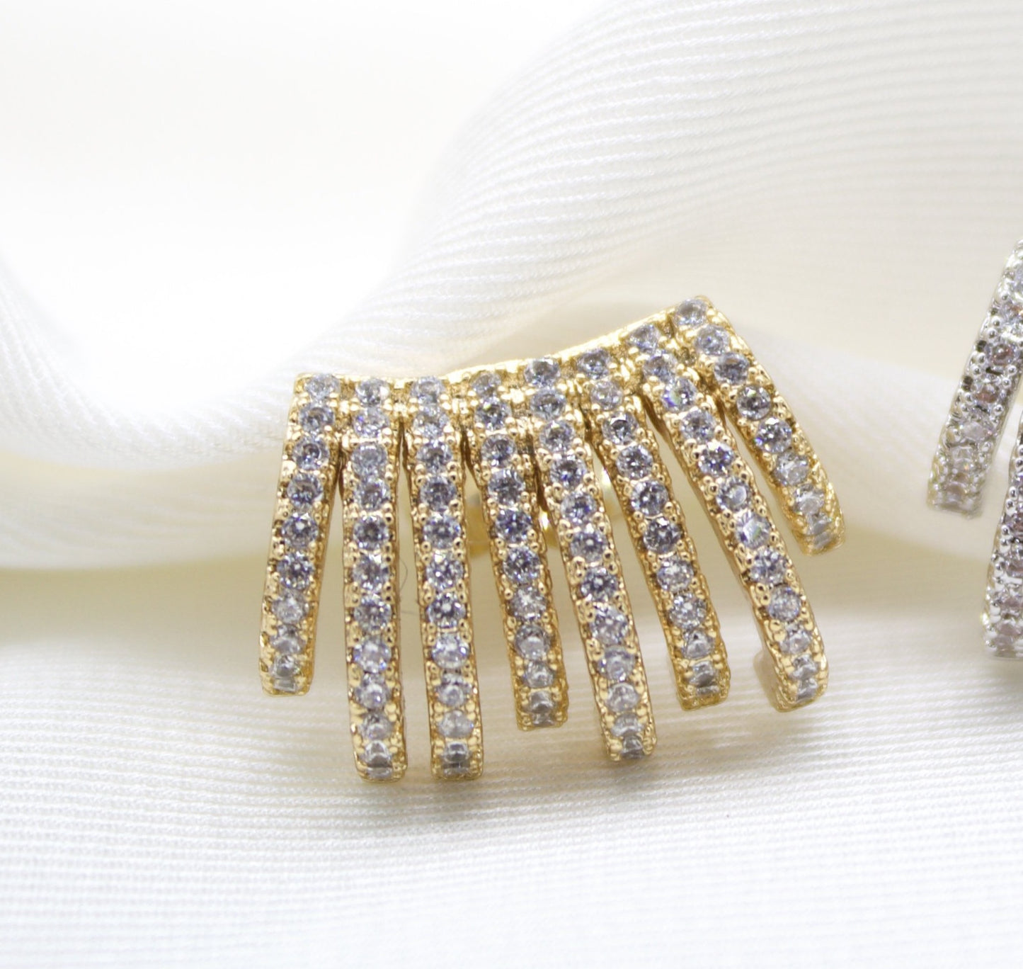 A gold multi-strand ear cuff encrusted with sparkling cubic zirconia stones rests elegantly on a soft white fabric background.