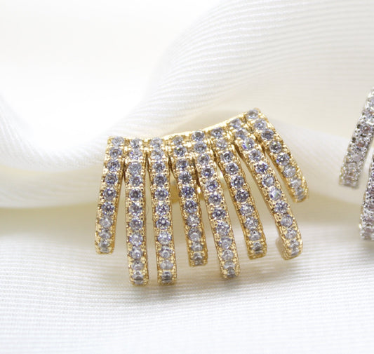 A gold multi-strand ear cuff encrusted with sparkling cubic zirconia stones rests elegantly on a soft white fabric background.