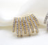 A gold multi-strand ear cuff encrusted with sparkling cubic zirconia stones rests elegantly on a soft white fabric background.