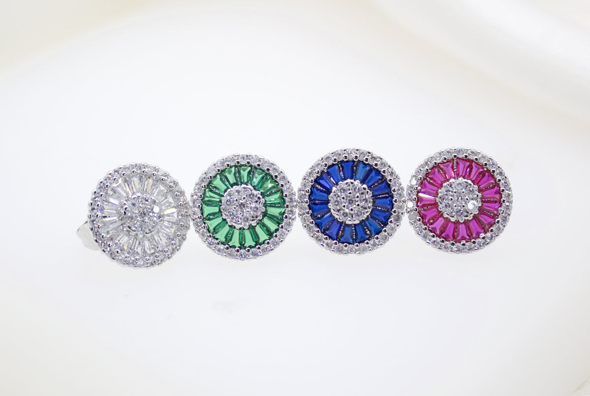 Four round sterling silver cluster rings sparkle on a white surface, each featuring a central halo of pave-set diamonds surrounded by baguette stones in clear, green, blue, and pink.