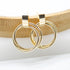 A pair of polished gold double-hoop earrings rests against a curved wooden display.
