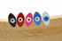Five colorful evil eye enamel stud earrings in black, red, pink, blue, and white display upright on a wooden surface.
