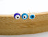 Three matching evil eye stud earrings in dark blue, light blue, and white rest on a curved wooden surface.