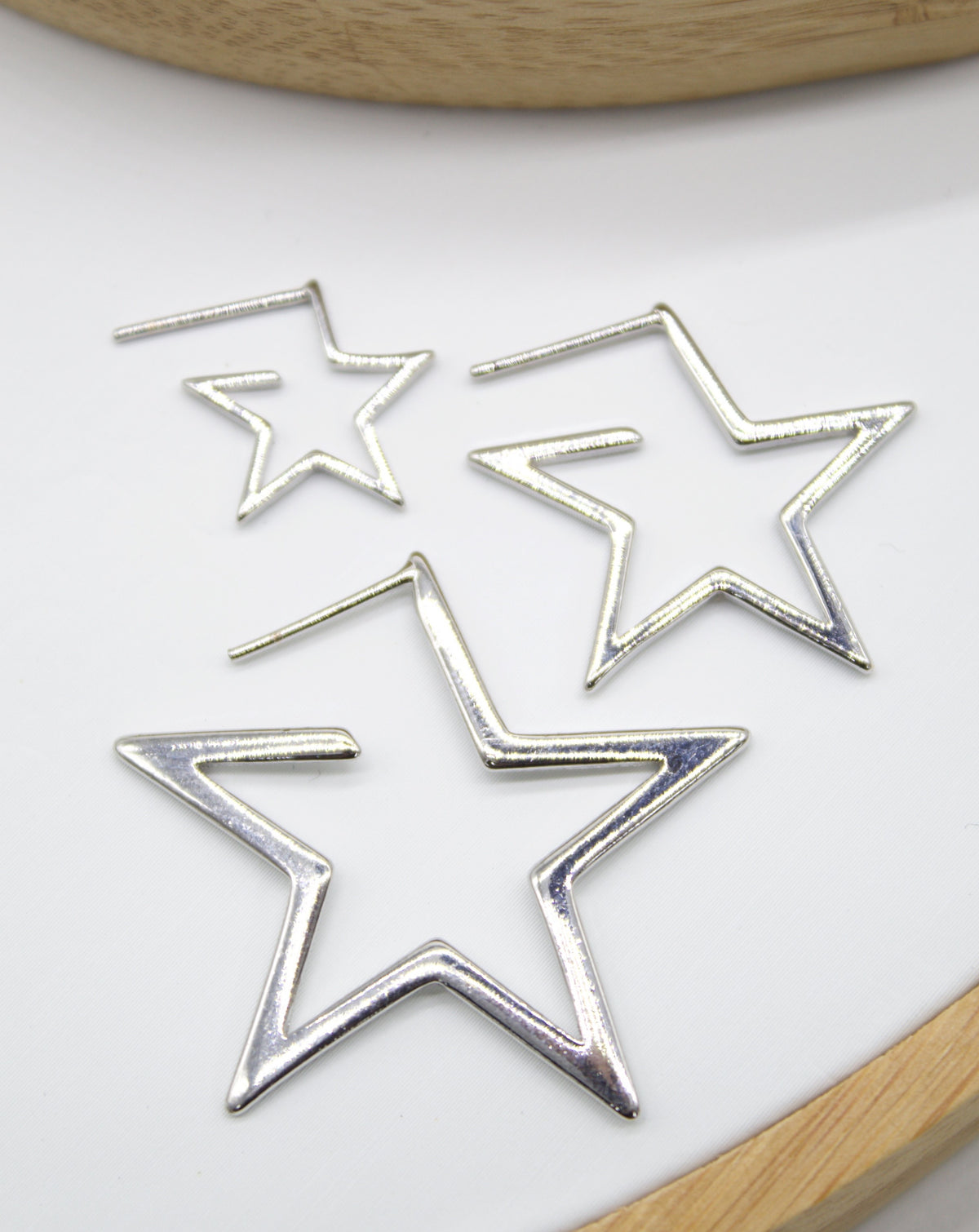 Three silver star-shaped hoop earrings of varying sizes rest against a clean white background.