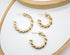 Three polished gold twisted hoop earrings rest on a white surface inside a wooden display tray.