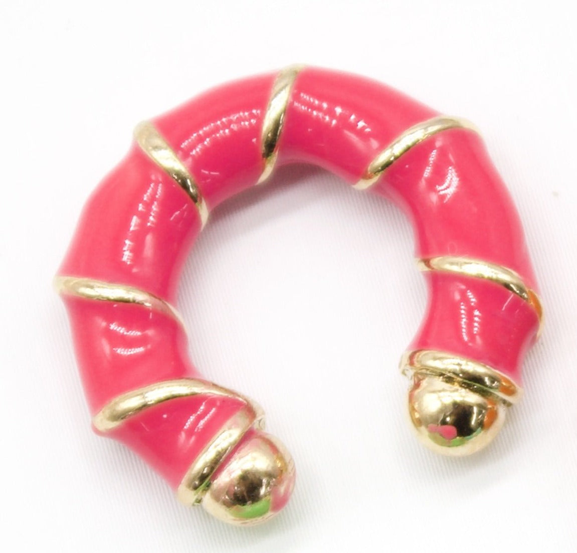 A chunky pink enameled hoop earring features gold bands wrapped around its body and polished gold ball terminals.