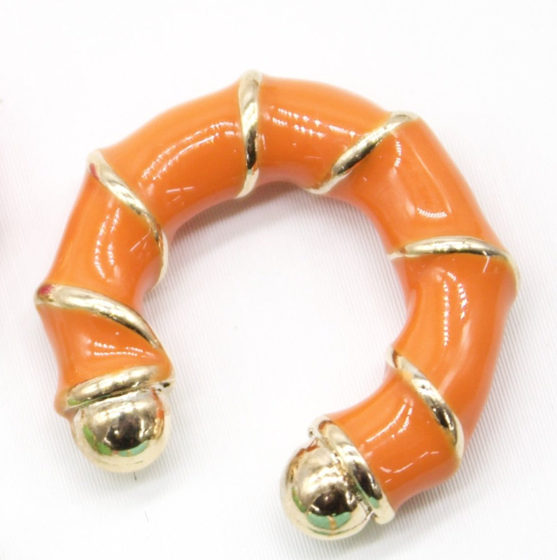 A vibrant orange enamel hoop earring features polished gold-tone bamboo accents and spherical ends.