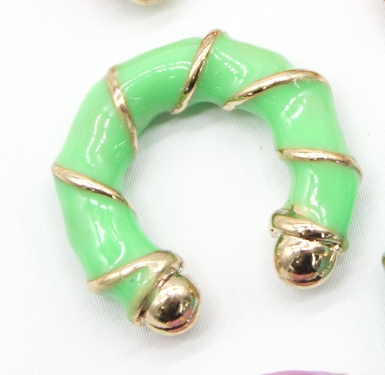 A bright green and gold enamel hoop earring rests against a white background.
