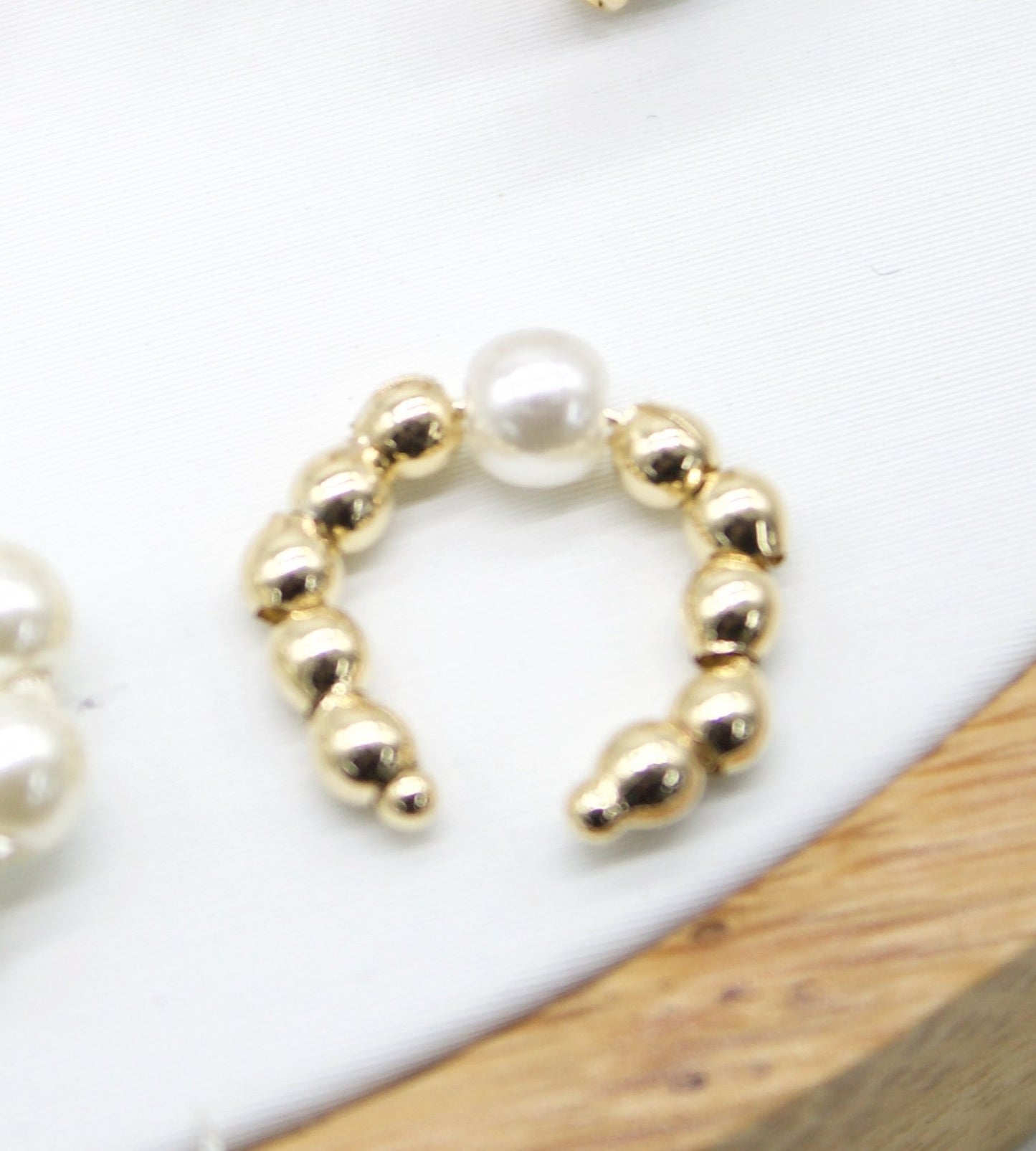 A gold beaded ear cuff features a central white pearl.
