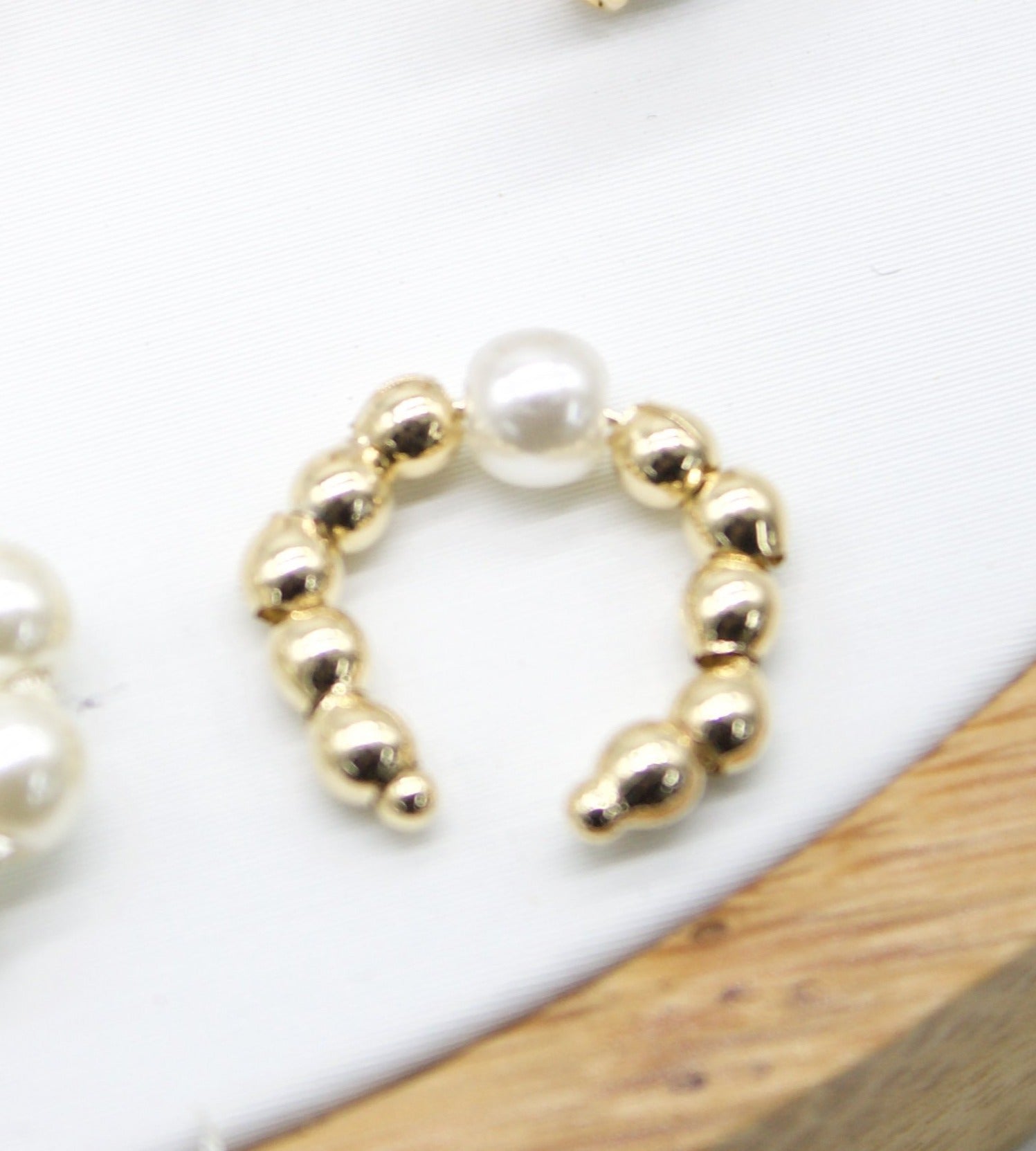 A gold beaded ear cuff features a central white pearl.