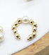 A gold beaded ear cuff features a central white pearl.